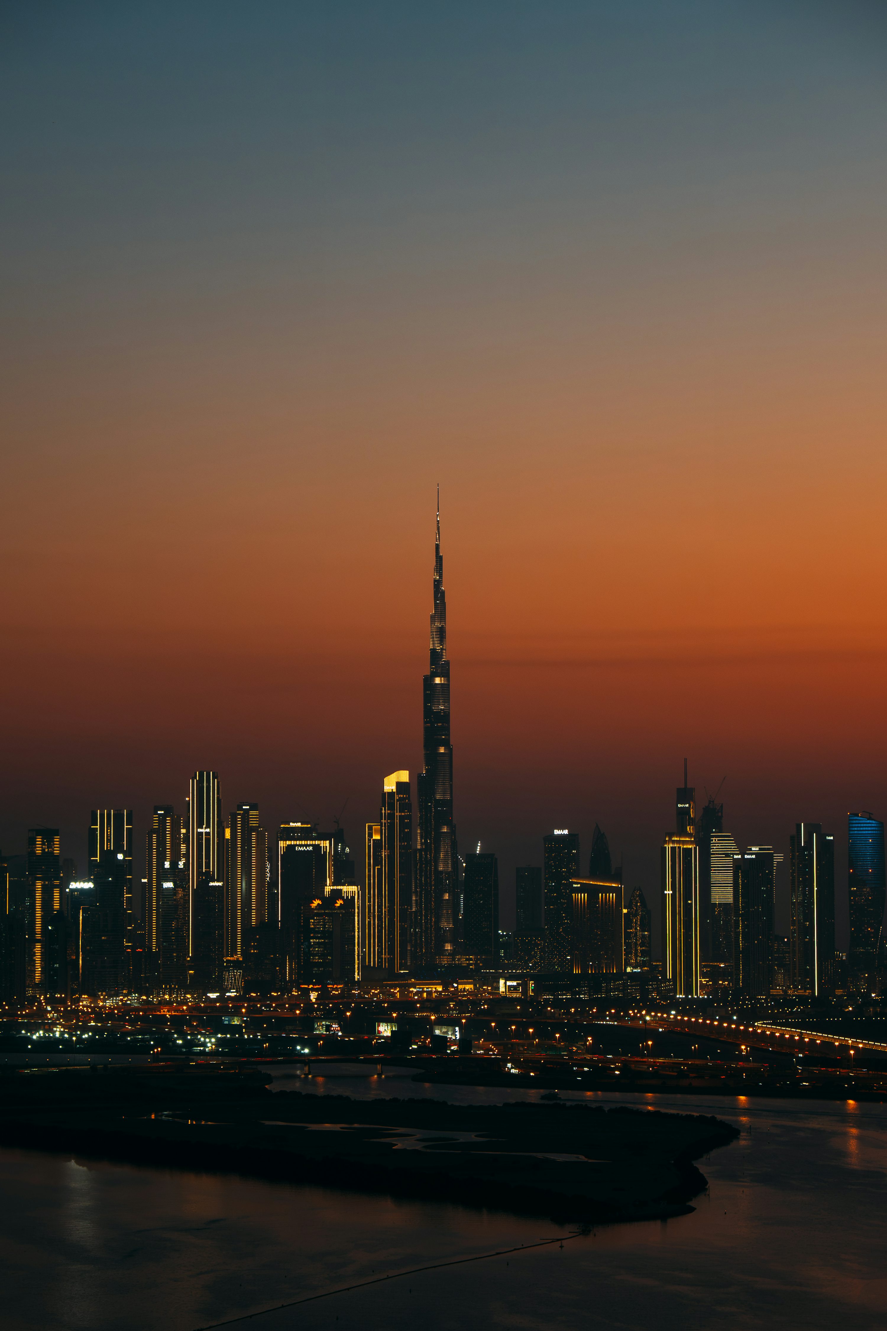 Vista de Dubai ao entardecer com prédios iluminados e céu alaranjado.