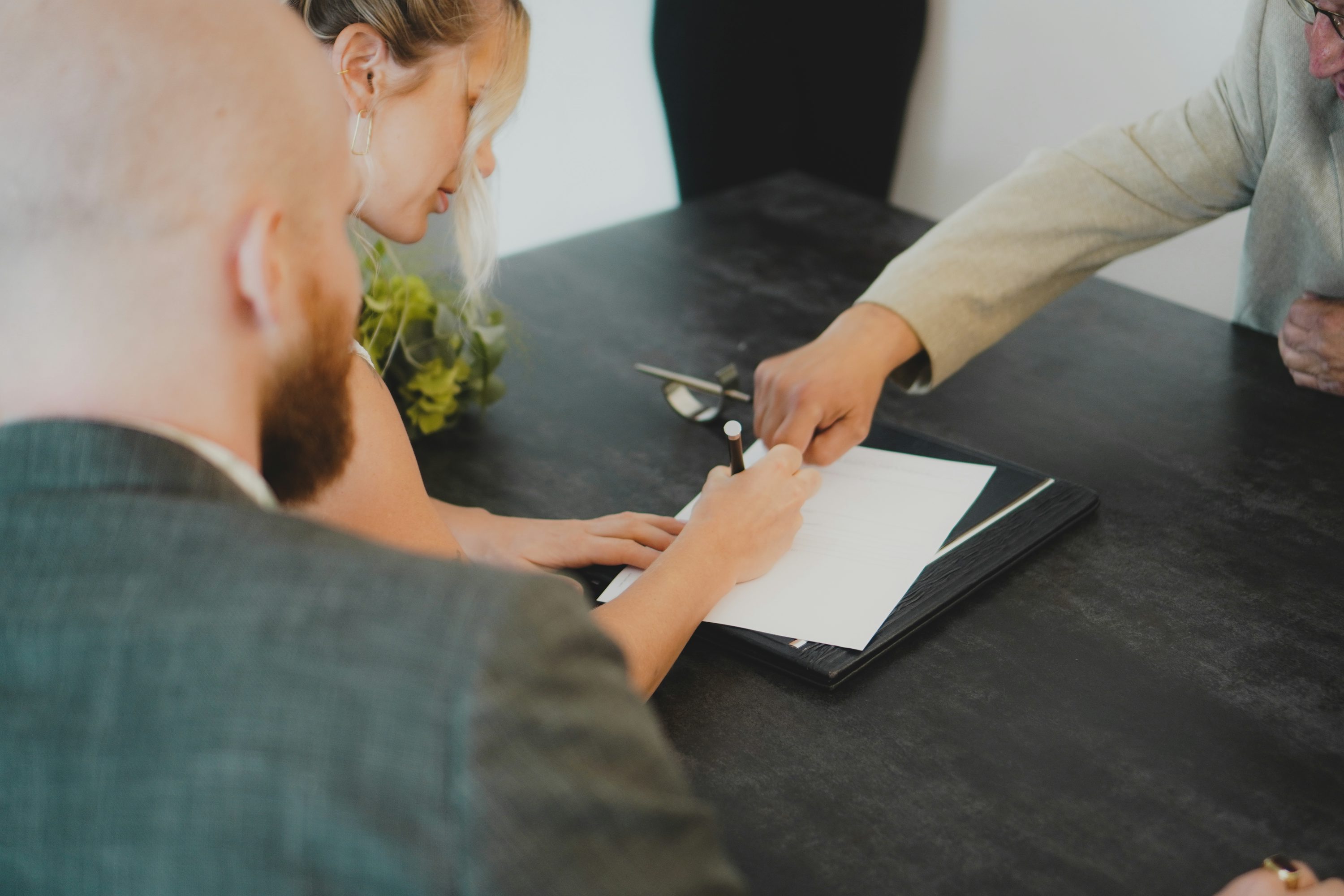 Pessoa apontando informações em um contrato sobre uma mesa escura.