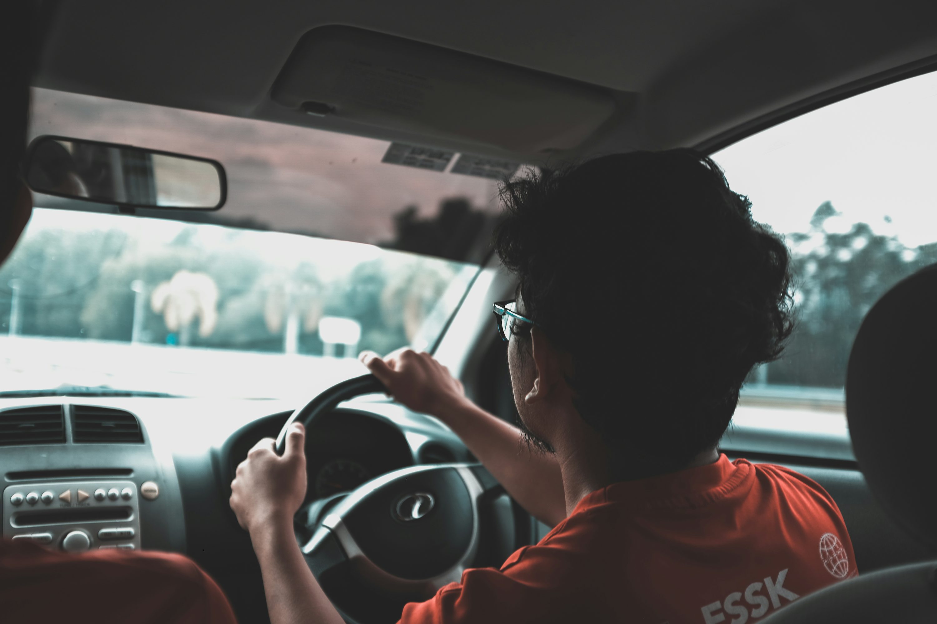 Pessoa dirigindo um carro vista pelo banco traseiro.