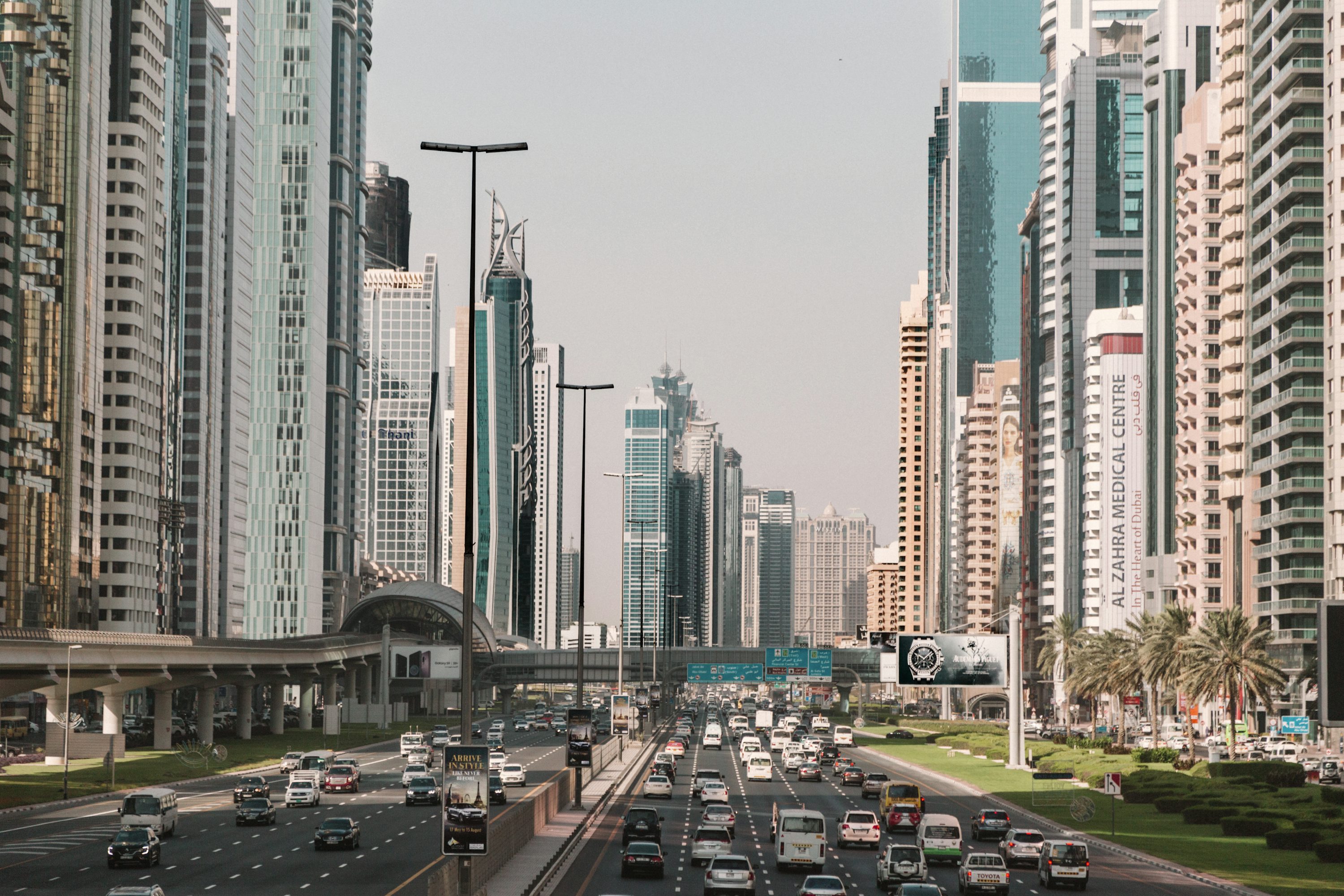 Avenida urbana de Dubai com edifícios, veículos e sinalização ao entardecer.