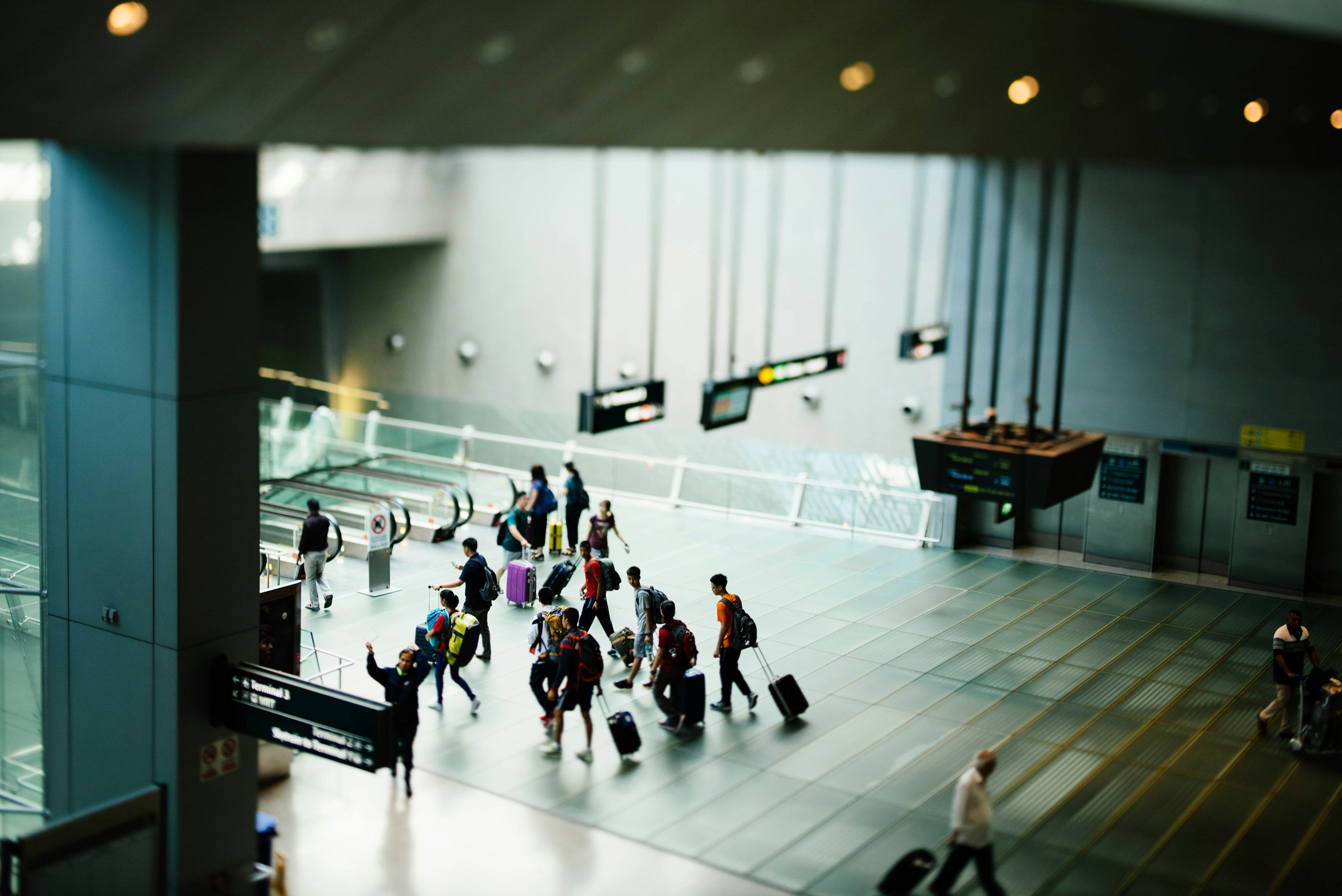 Pessoas caminhando em corredor de aeroporto com malas.