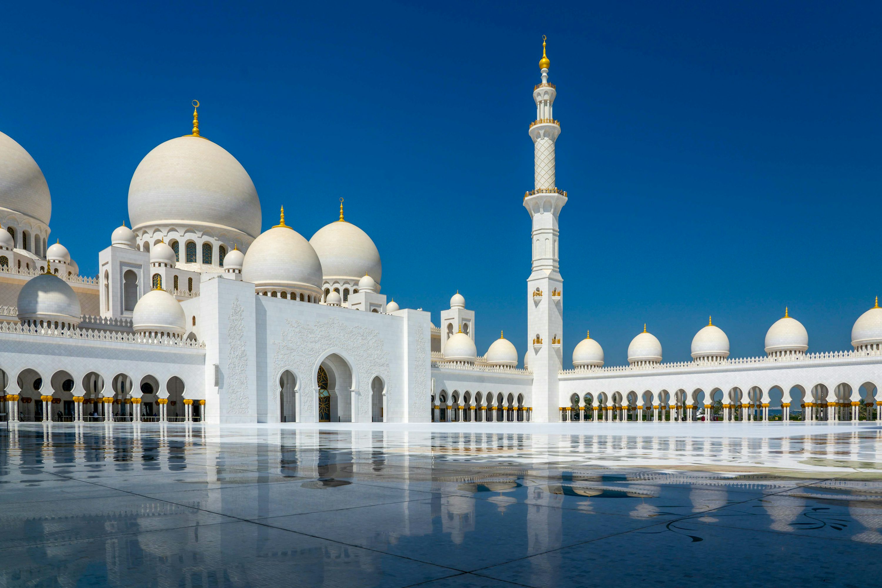 Grande mesquita de cúpulas brancas sob céu azul nos Emirados Árabes Unidos.