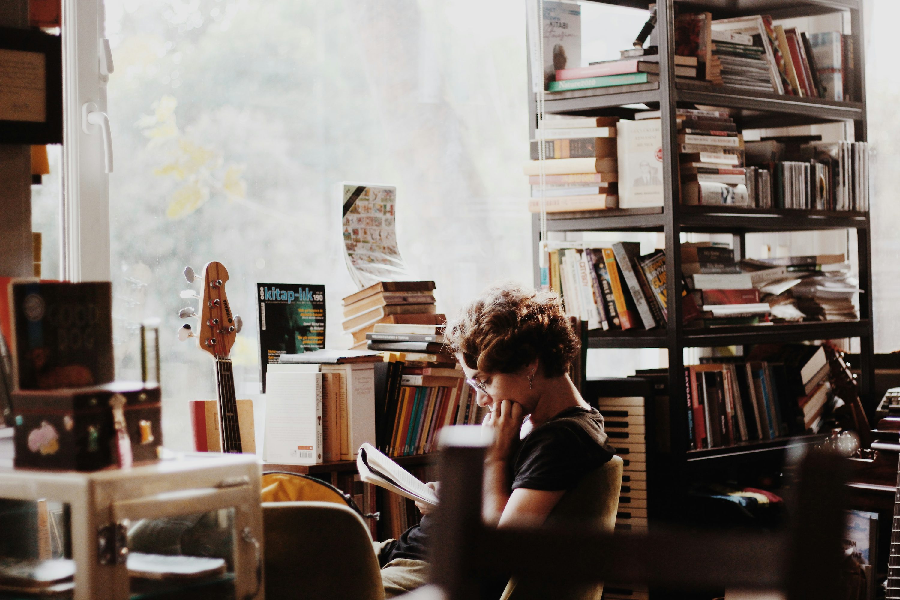 Pessoa estudando em biblioteca com livros e mesas de leitura.