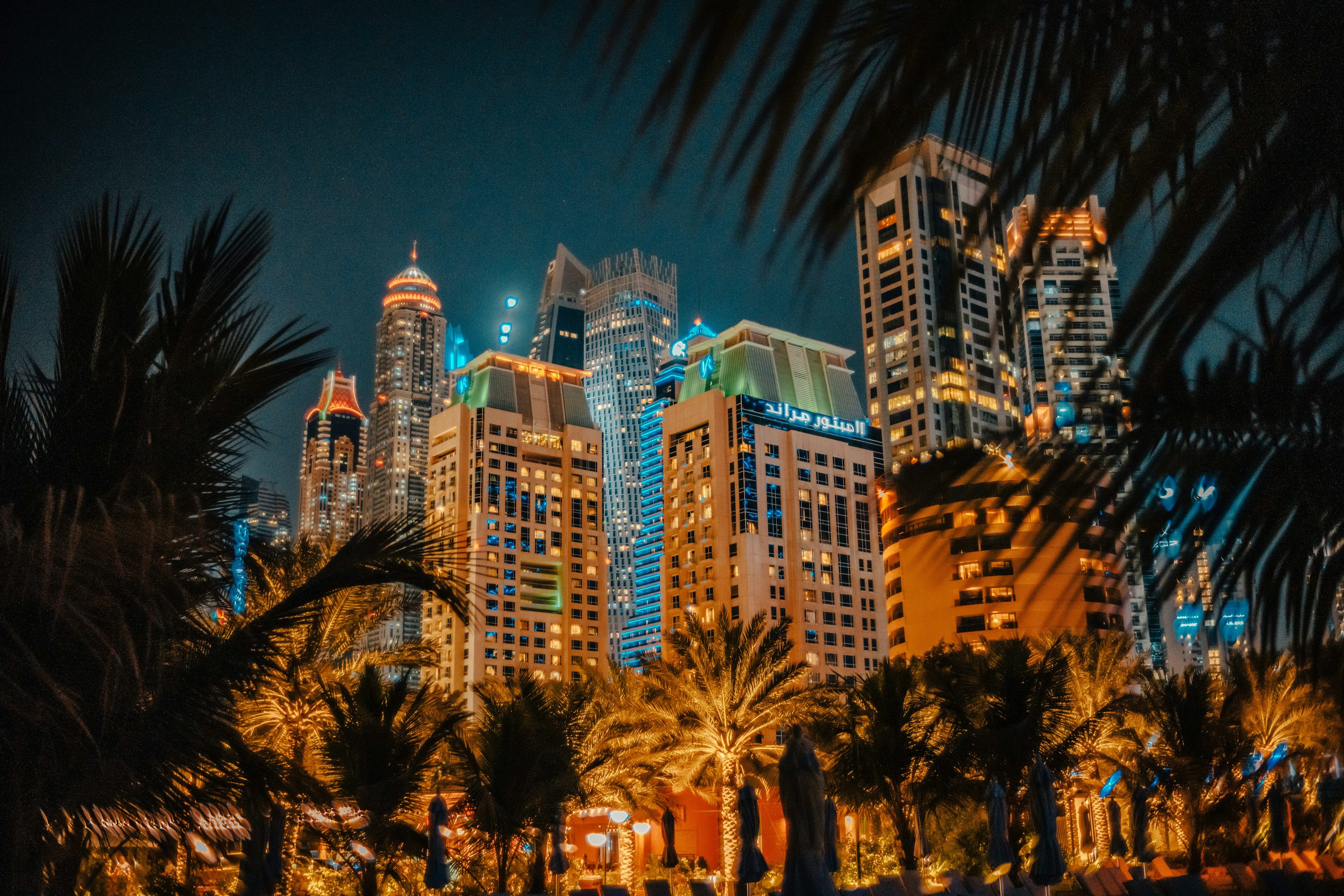 Edifícios de Dubai iluminados à noite entre palmeiras.