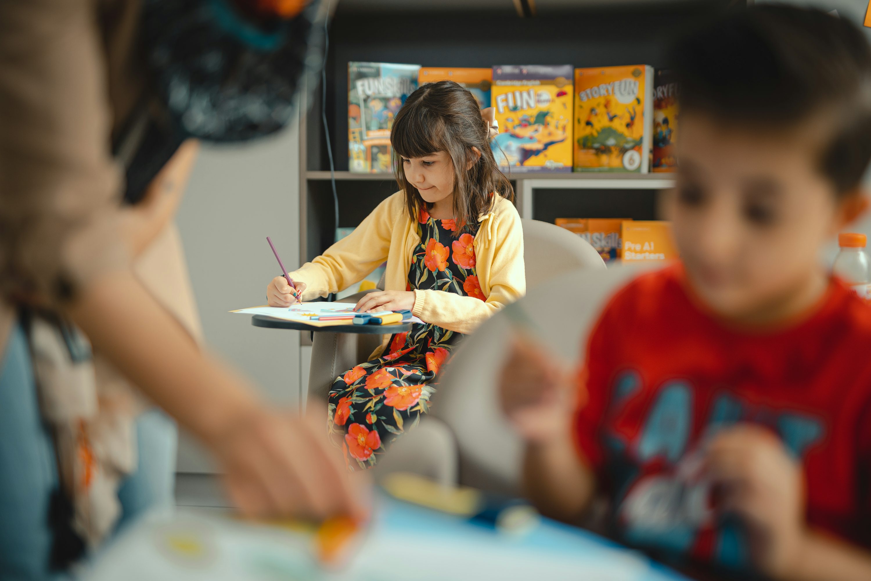 Crianças desenhando em mesa de sala de aula com materiais coloridos.