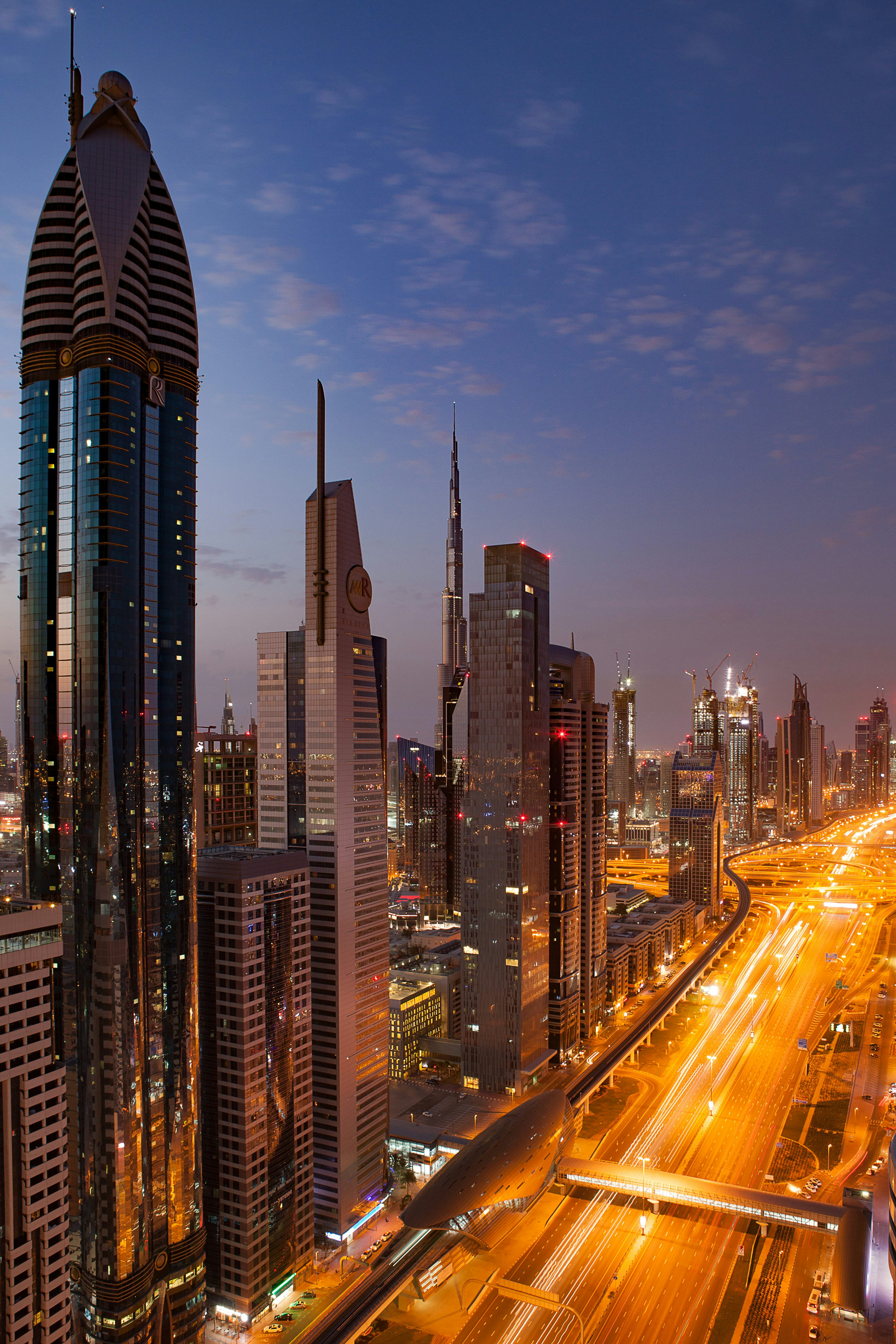 Avenida de Dubai ao amanhecer com edifícios altos e fluxo de veículos.